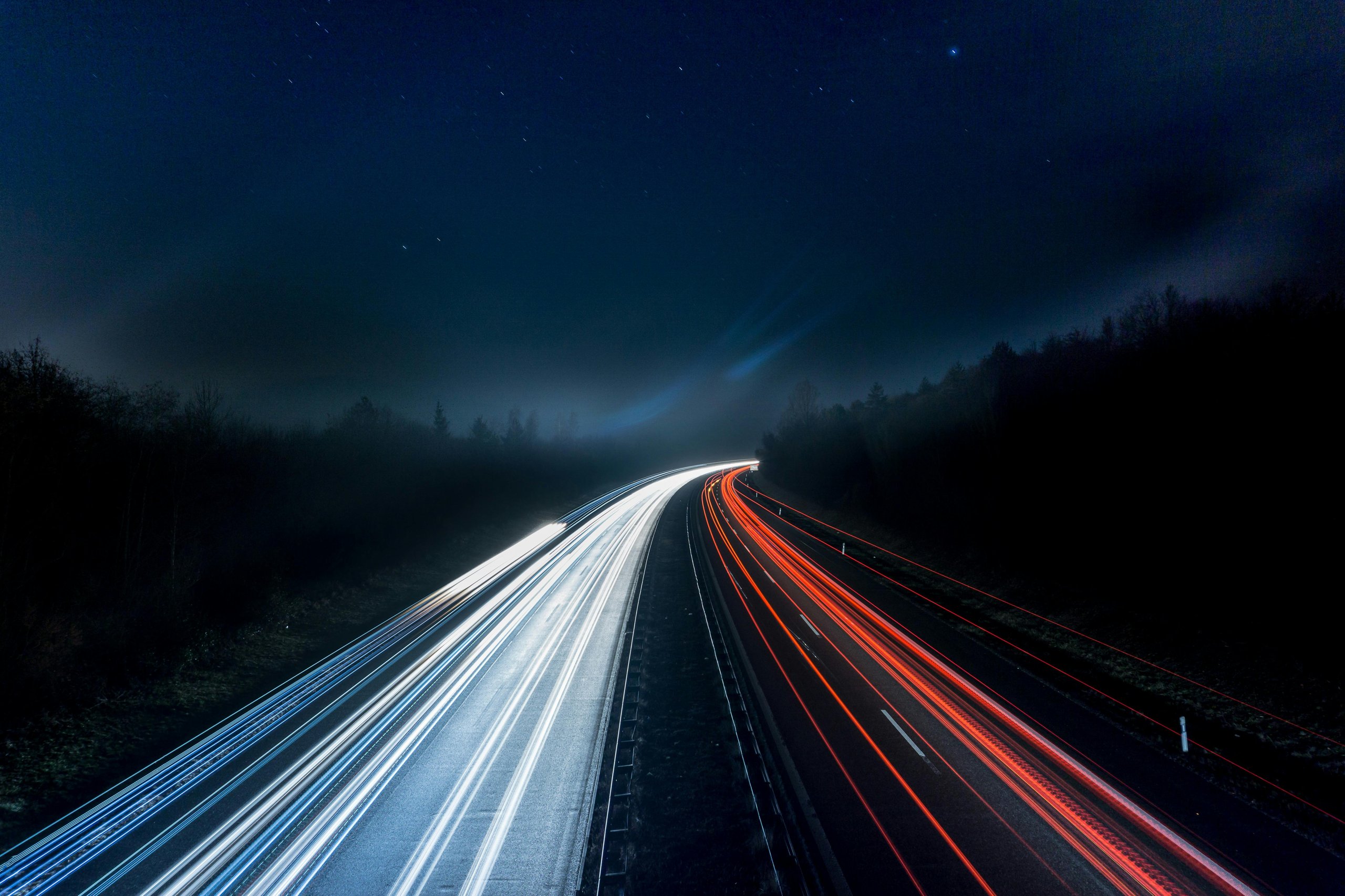 Long exposure of a highway at night showing white and red light trails from moving vehicles.