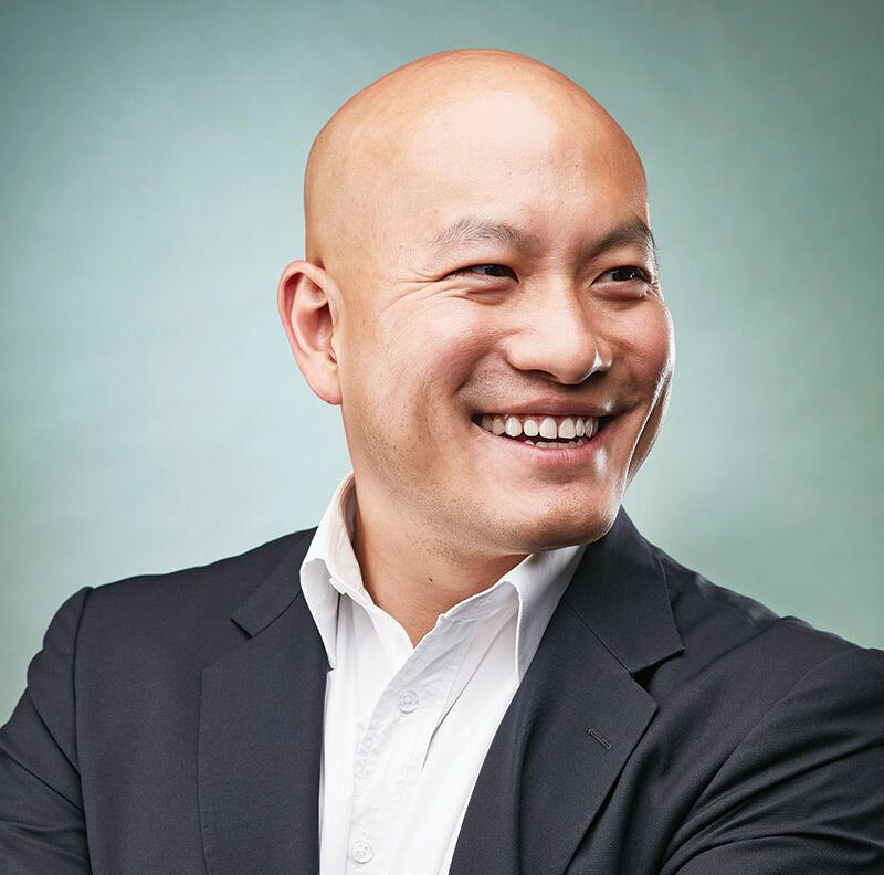 Smiling bald man wearing a white shirt and dark blazer looking to the right.