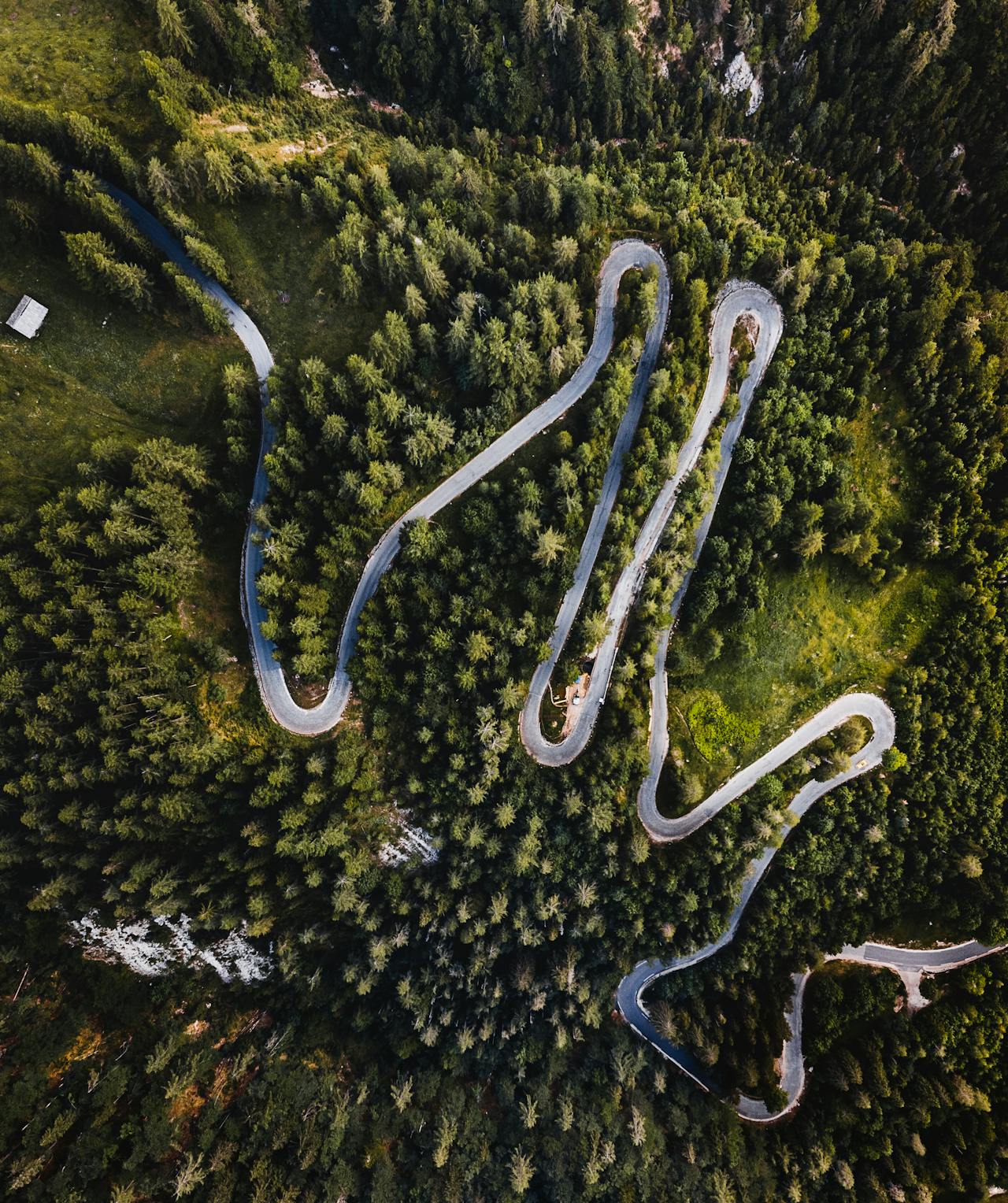 Aerial view of a winding mountain road cutting through dense green forest.