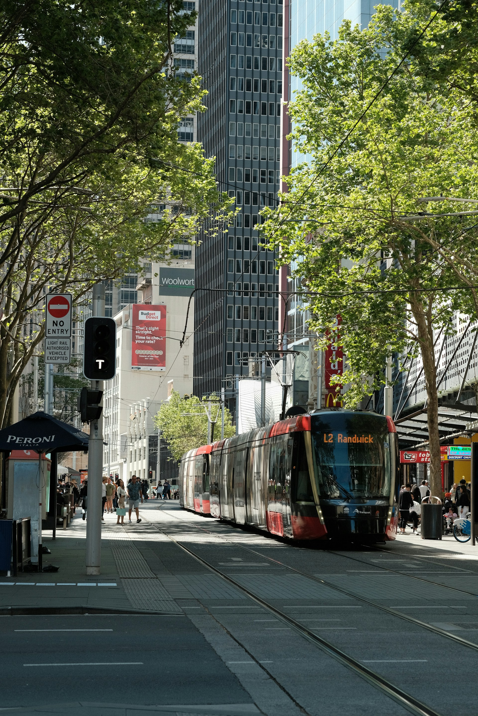 Modern light rail tram travelling through a city street lined with buildings and trees