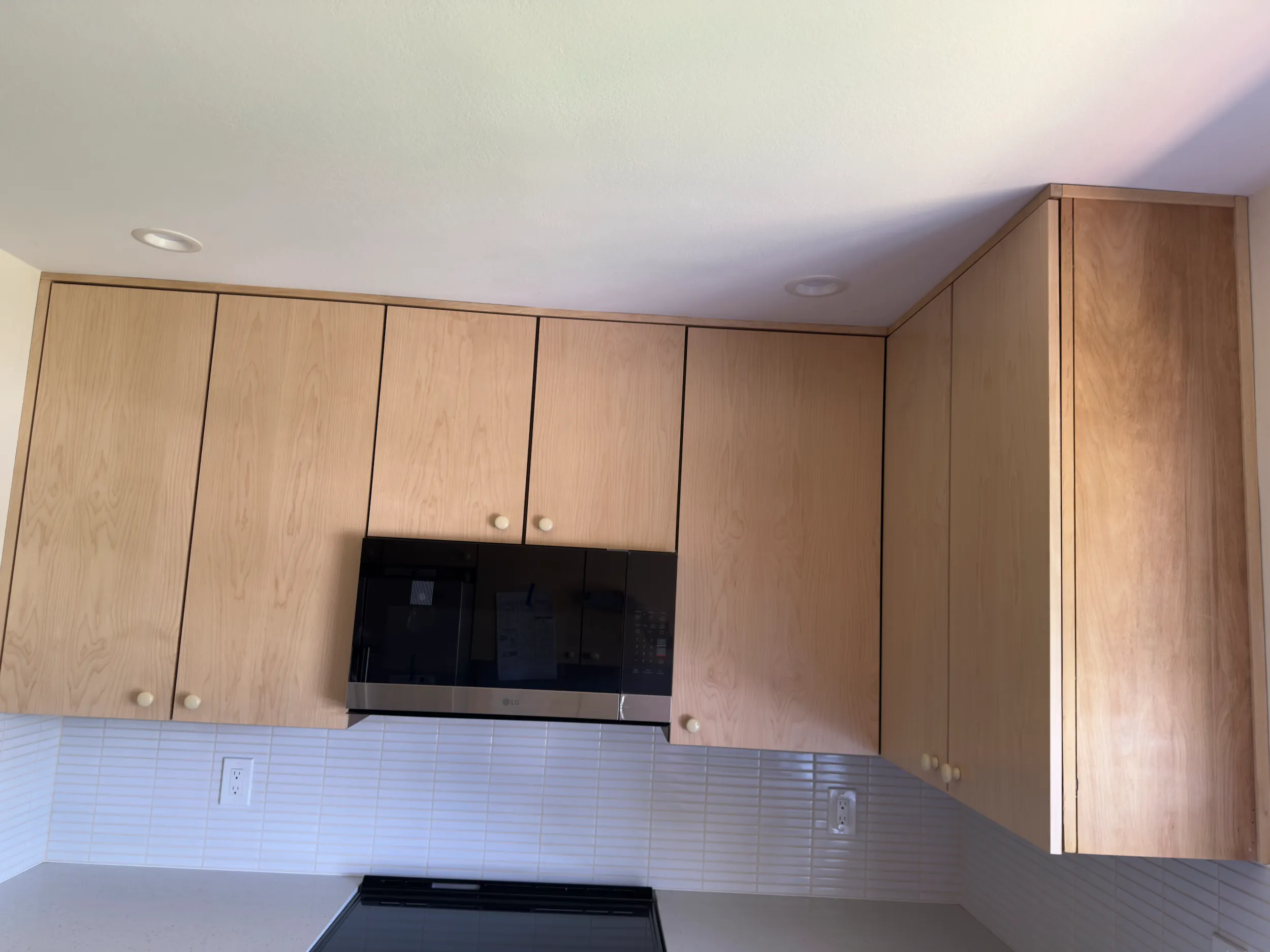 Custom kitchen cabinet panels with wood grain finish, tile backsplash, and microwave hood.