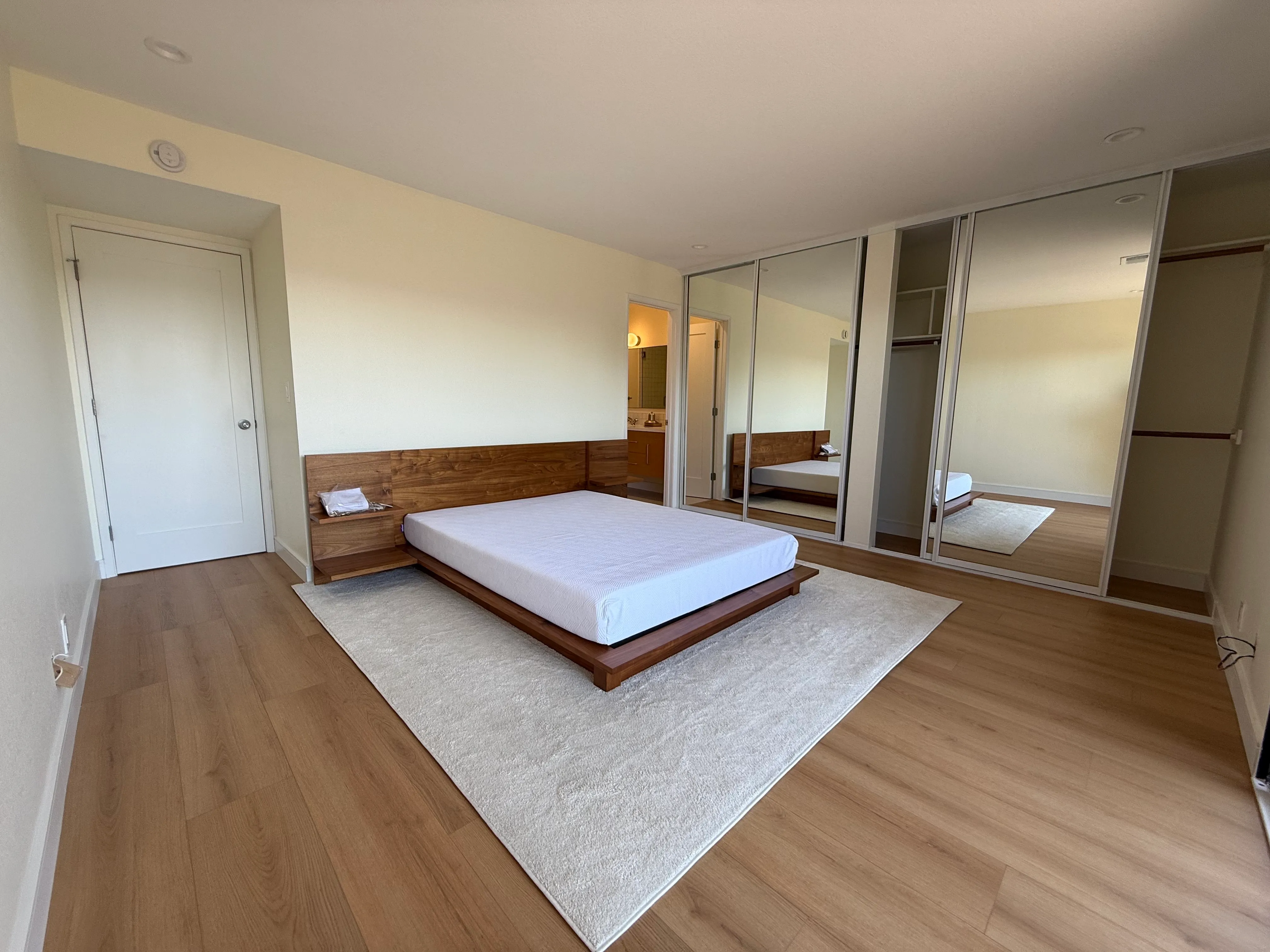 Remodeled bedroom with new flooring, painted walls, interior door, mirrored sliding closet doors, and finished trim.