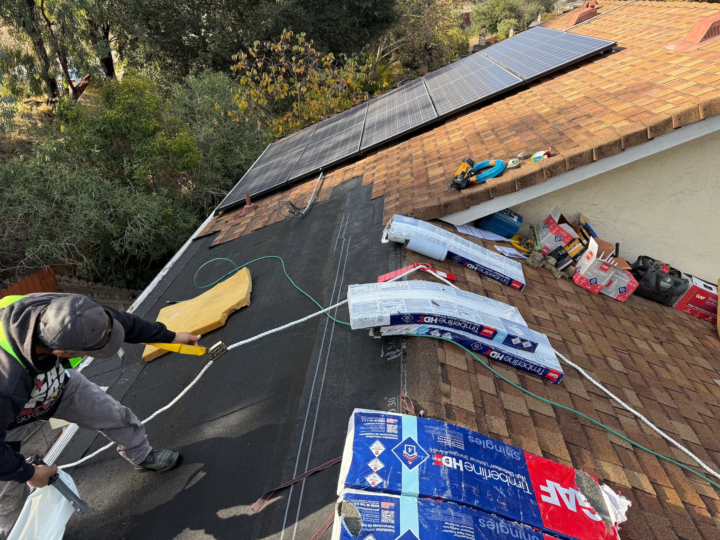Roof repair in progress with underlayment, shingles, solar panels, and weatherproofing materials.