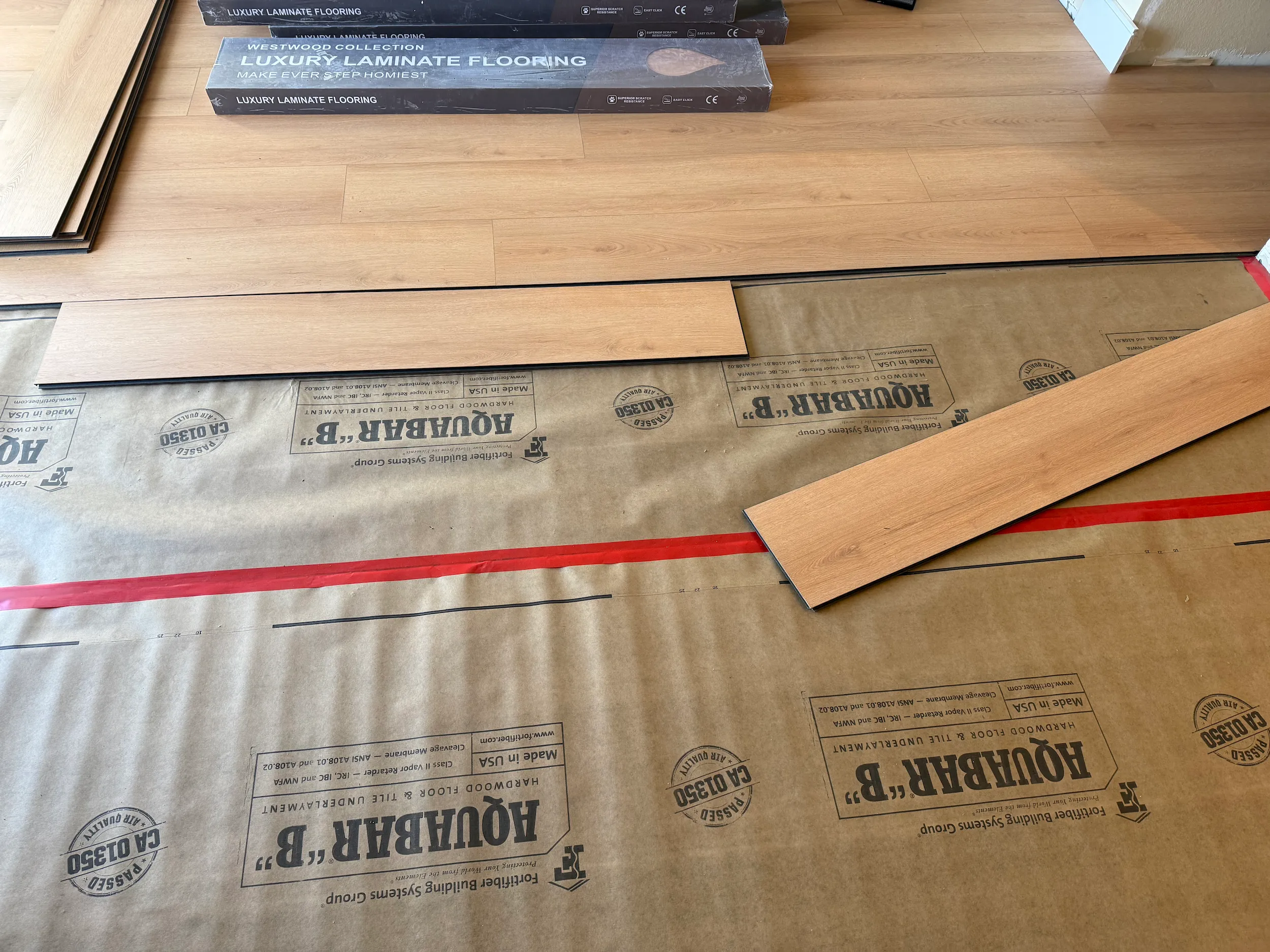 Laminate flooring installation in progress over underlayment with wood-look planks being laid out.