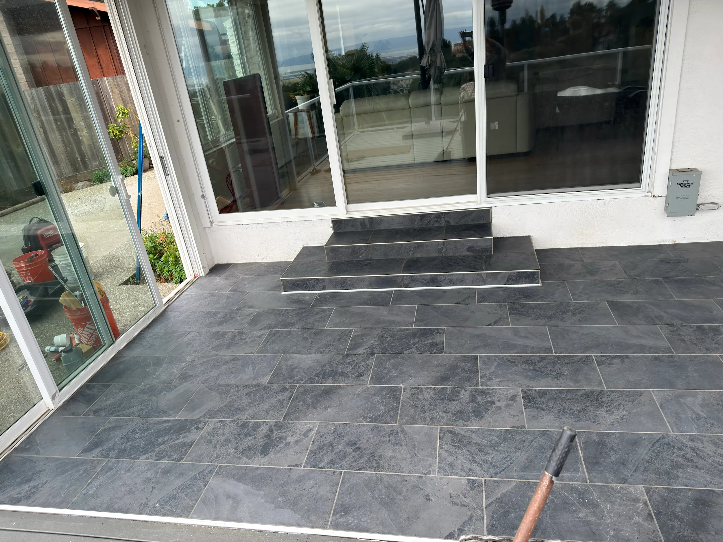 Finished gray tile surface with clean layout, grout lines, and tiled step transitions near sliding doors.