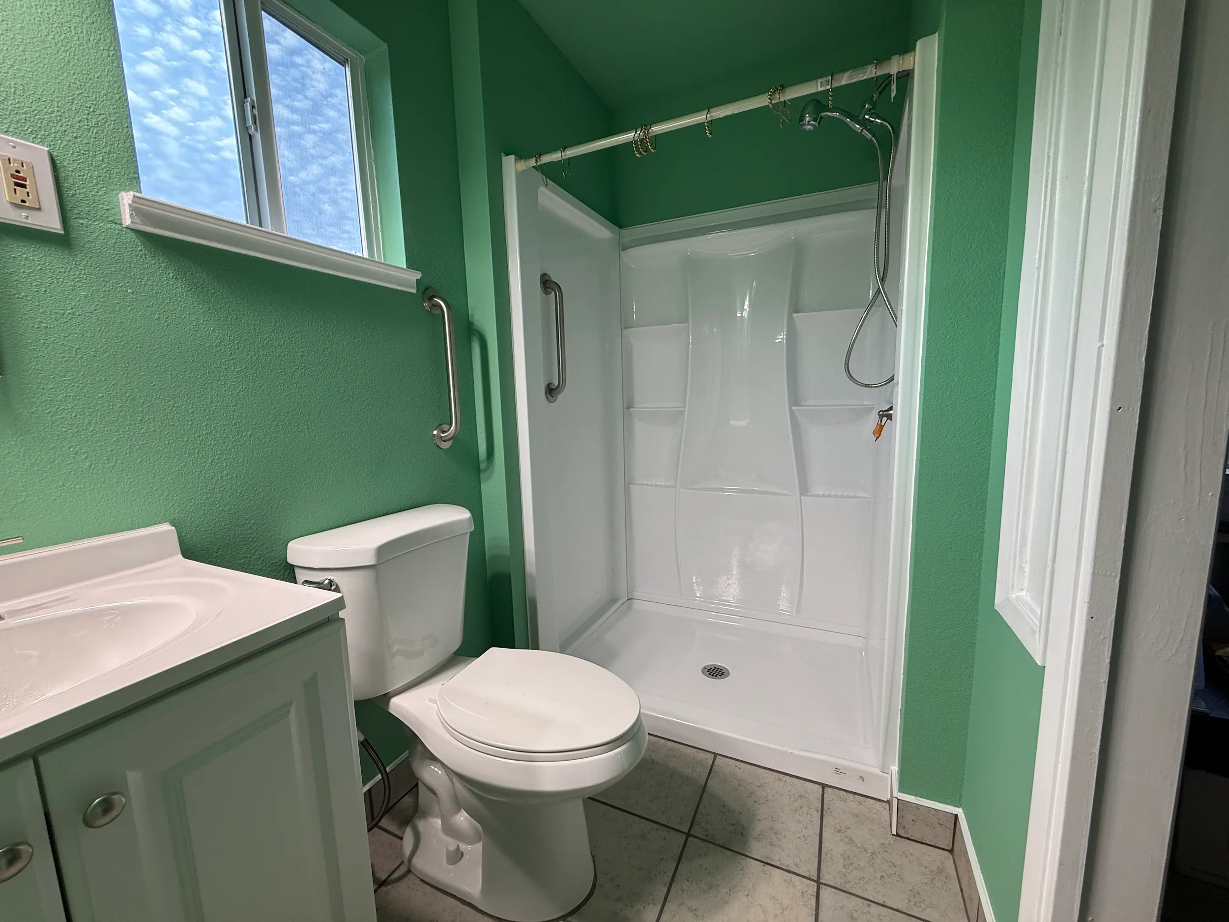 Finished bathroom with green painted walls, white trim, shower surround, vanity, and interior wall finishes.