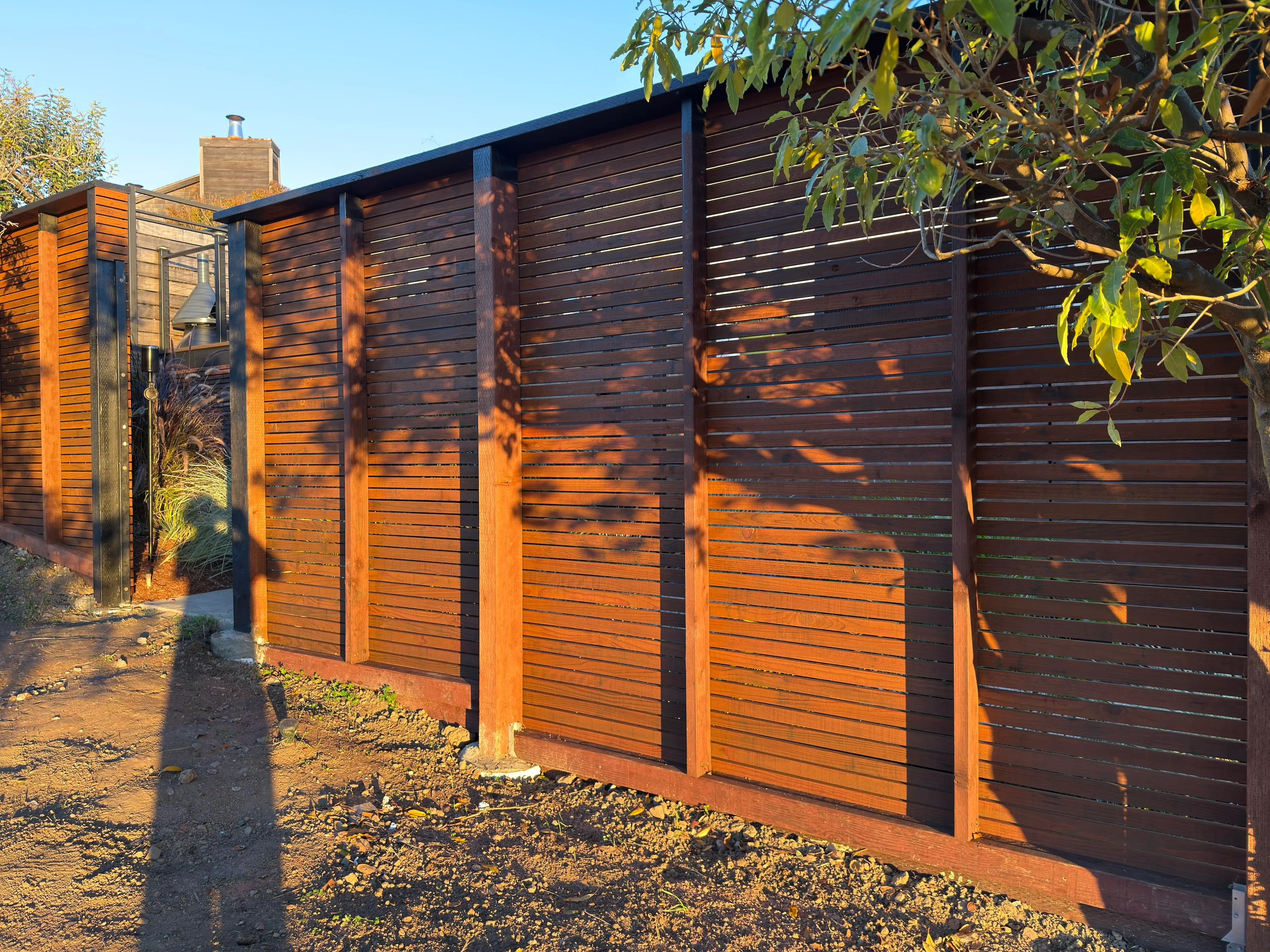 Custom horizontal wood fence with stained slats, wood posts, and integrated gate detail in an outdoor residential setting.