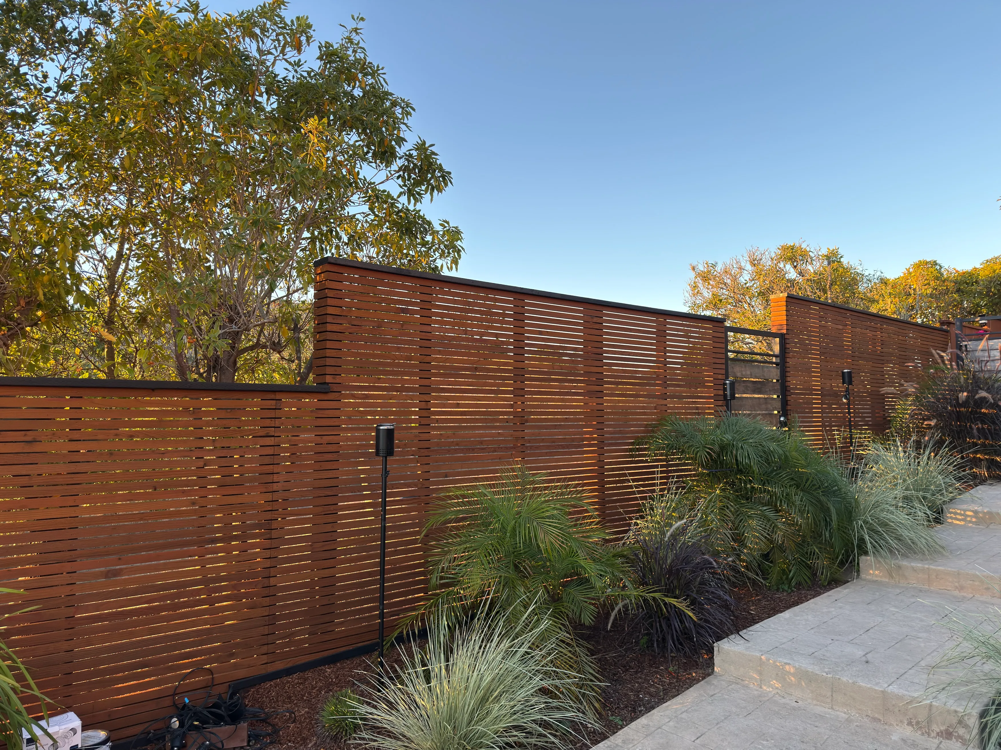 Custom horizontal wood fence with stained slats, integrated gate opening, and landscaped planting bed beside exterior steps.
