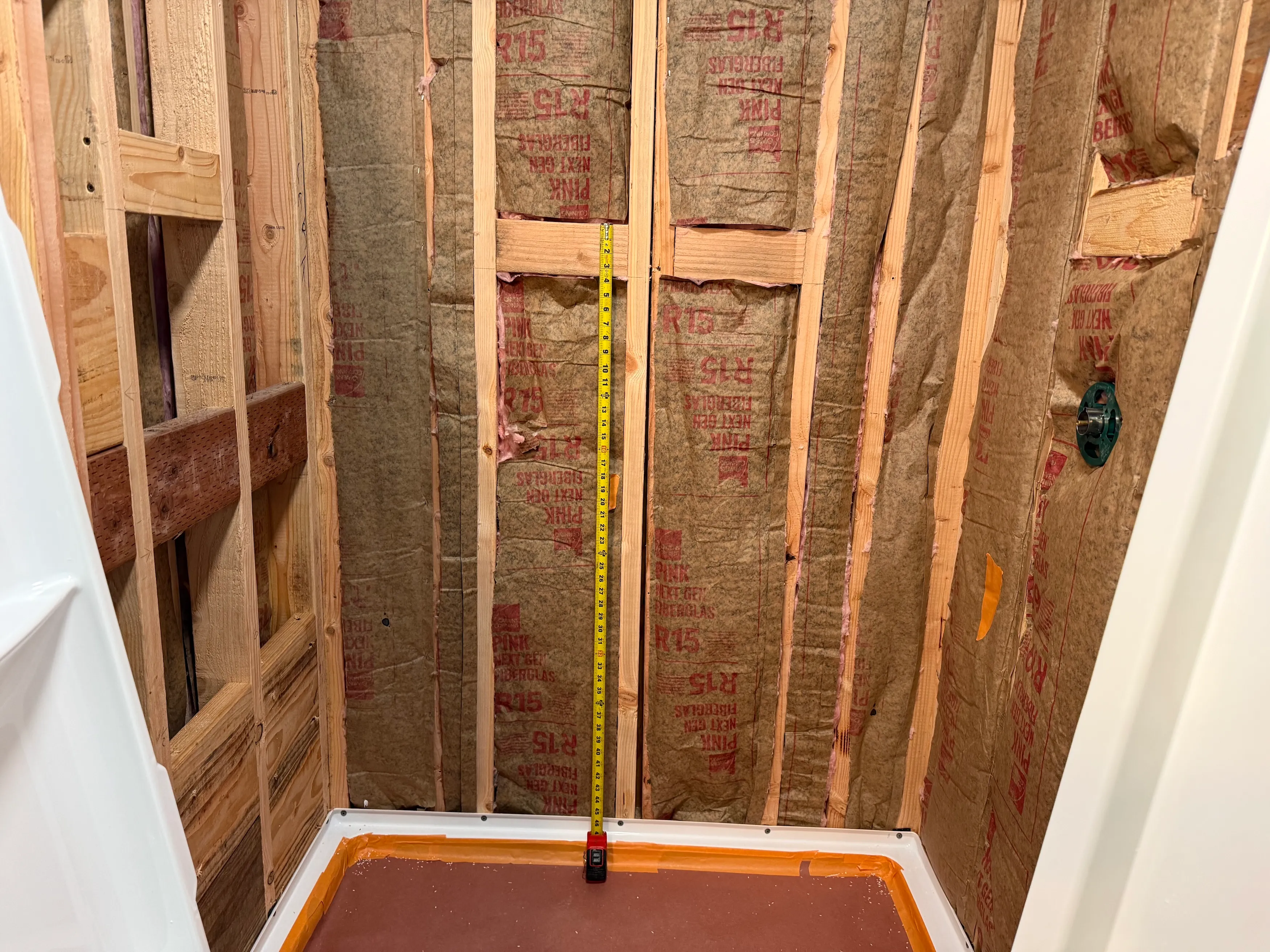 Bathroom wall framing with exposed studs, insulation, blocking, and backing preparation before waterproofing and shower finishes.