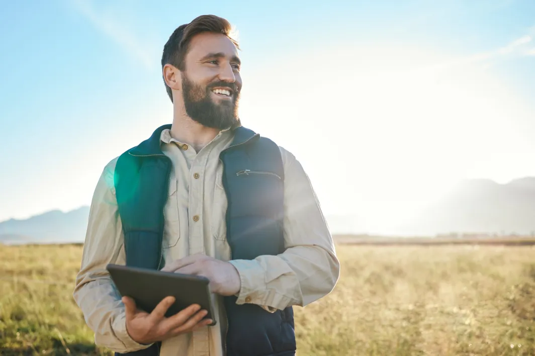 Smiling man holding a tablet standing in a farm field