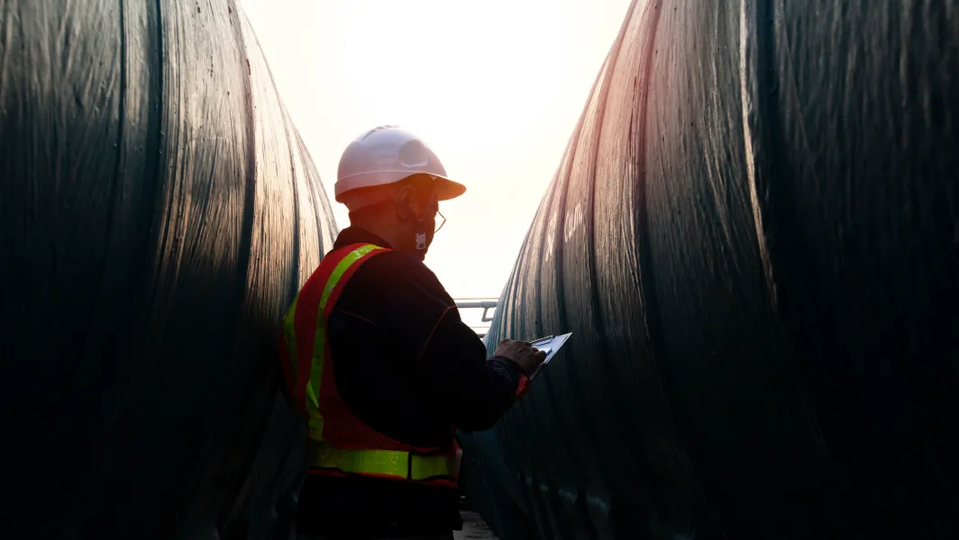 Man in safety gear holding a tablet while standing between large columns