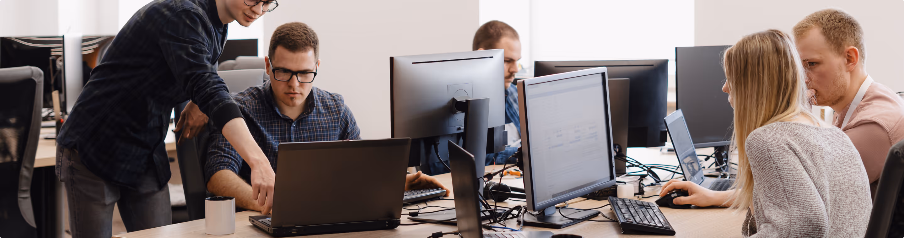 Team of young professionals collaborating and working on computers in an open office setting.