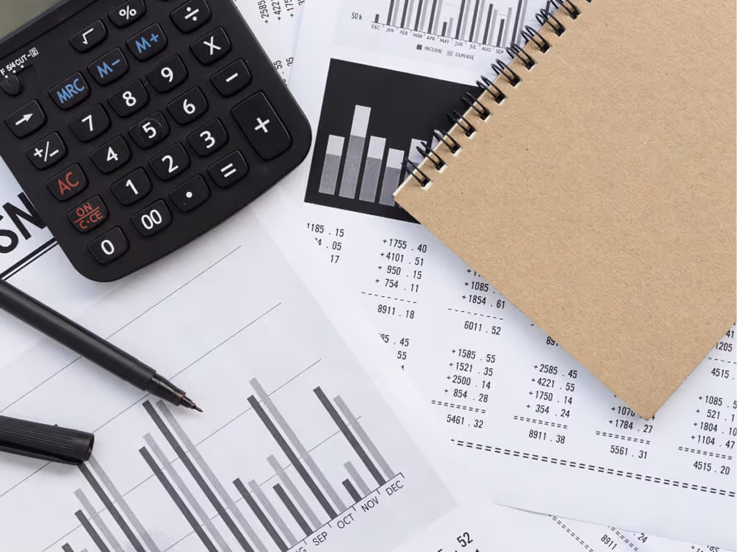 Calculator, black pen, spiral notebook, and financial documents with bar graphs and numerical data.