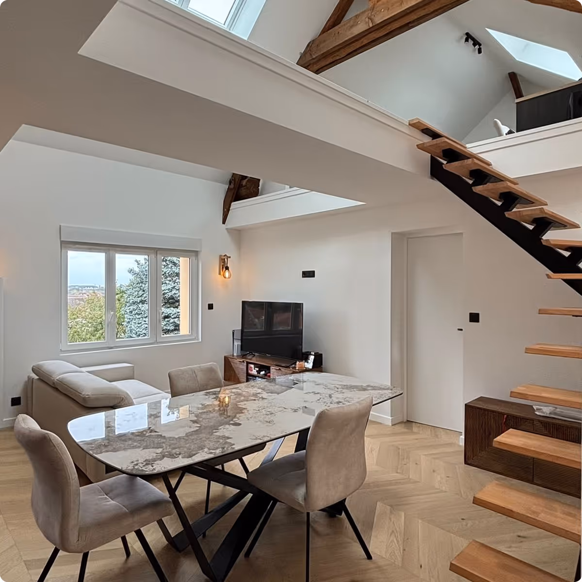 Modern living room with a marble dining table, four beige chairs, a beige sofa, TV on a wooden stand, and a wooden staircase leading to a loft.