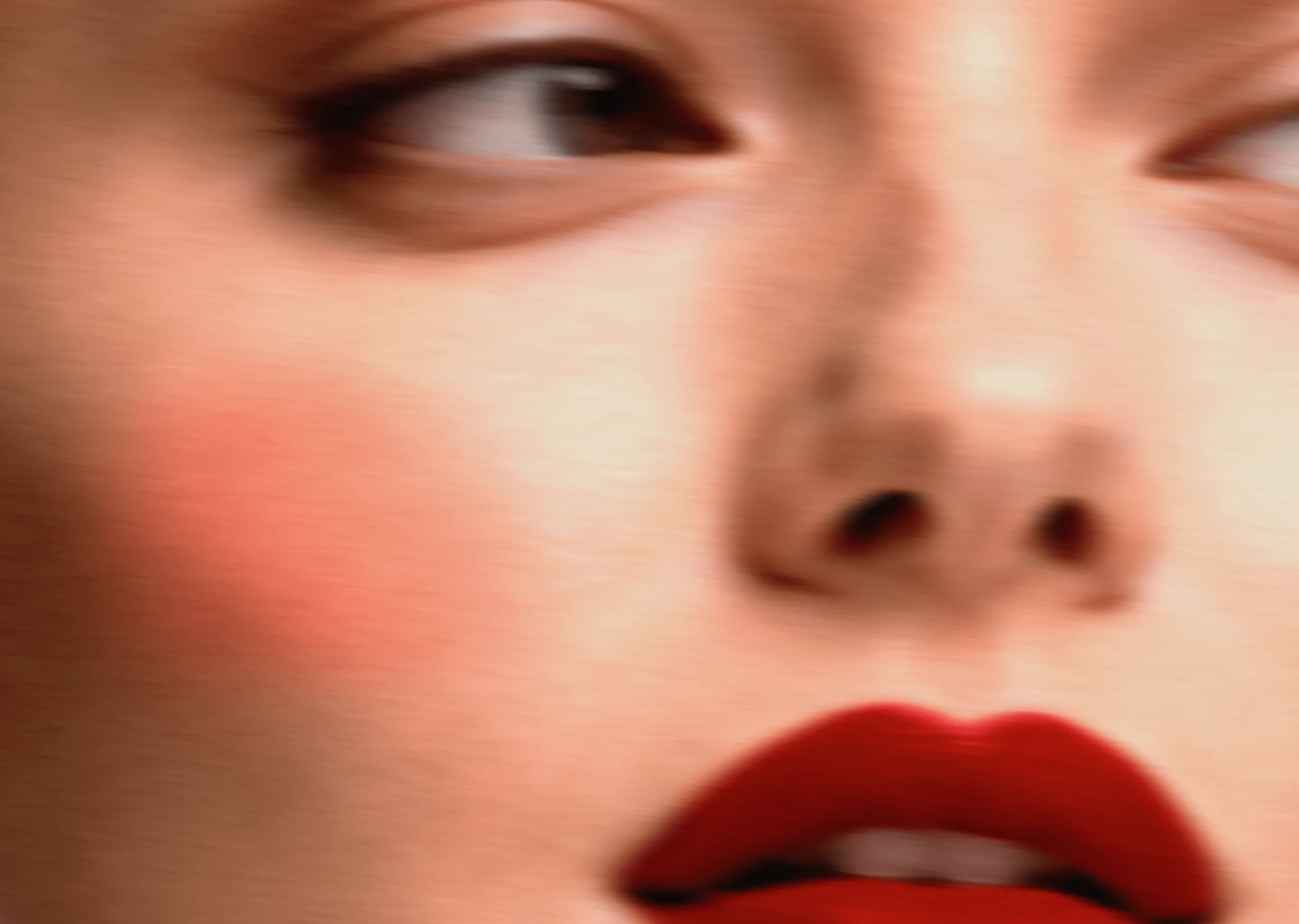 Close-up of a woman's face with bright red lipstick and a slight blush on her cheek, looking to the side.