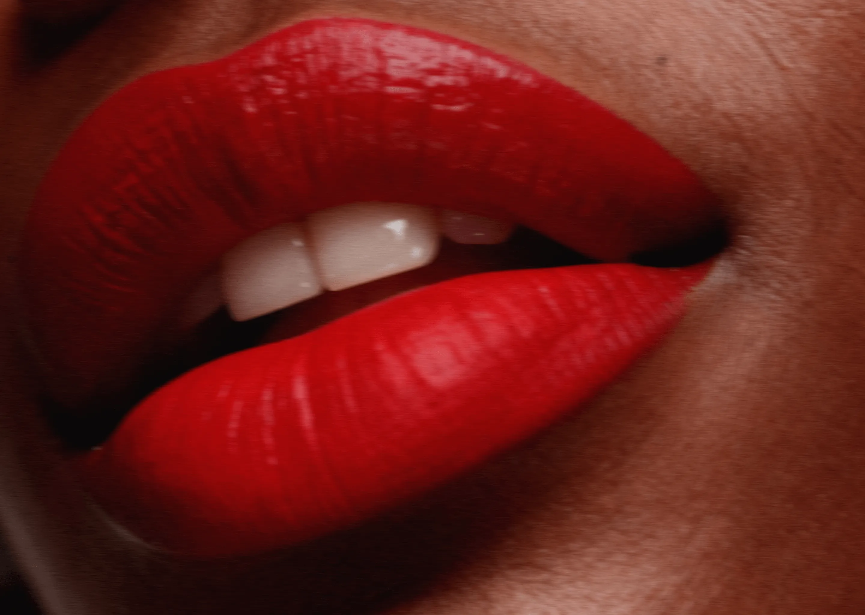 Close-up of lips with glossy red lipstick and visible white teeth.
