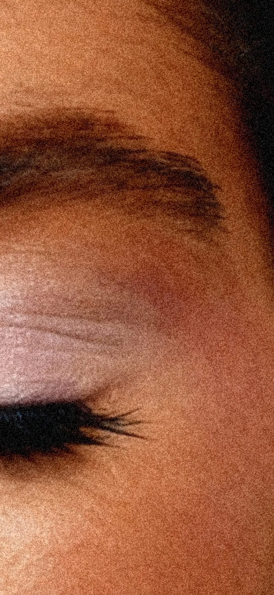 Close-up of a closed eye with thick eyelashes and a well-defined eyebrow on smooth skin.