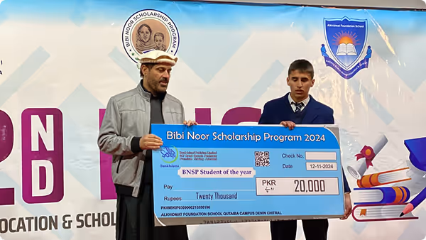 Two men holding a large ceremonial check for the Bibi Noor Scholarship Program 2024, with an amount of PKR 20,000 payable to BNSP Student of the Year.