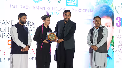 Four people on stage during the 1st Dast Aman Scholarship Program 2025, with one person presenting a plaque to another.