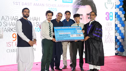 Five men on stage holding a large scholarship check, with a 1st Dast Aman Scholarship Program 2025 banner behind them.