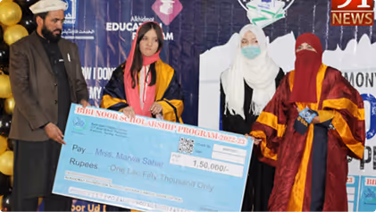 Four people on stage in graduation attire holding a large scholarship check during a ceremony.