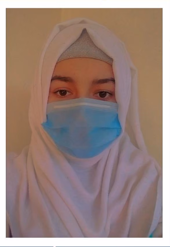 Person wearing a white hijab and a blue surgical mask covering nose and mouth.