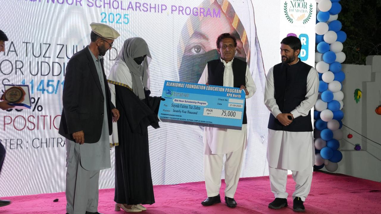 Four people on stage during a scholarship award ceremony, one woman in a veil holding a large check for 75,000 PKR from Alkidmat Foundation Education Program.