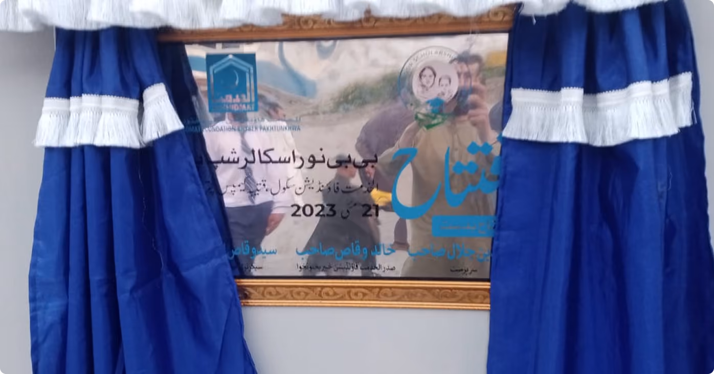 Blue curtains with white fringes framing a commemorative plaque in Urdu celebrating an event held on May 21, 2023.