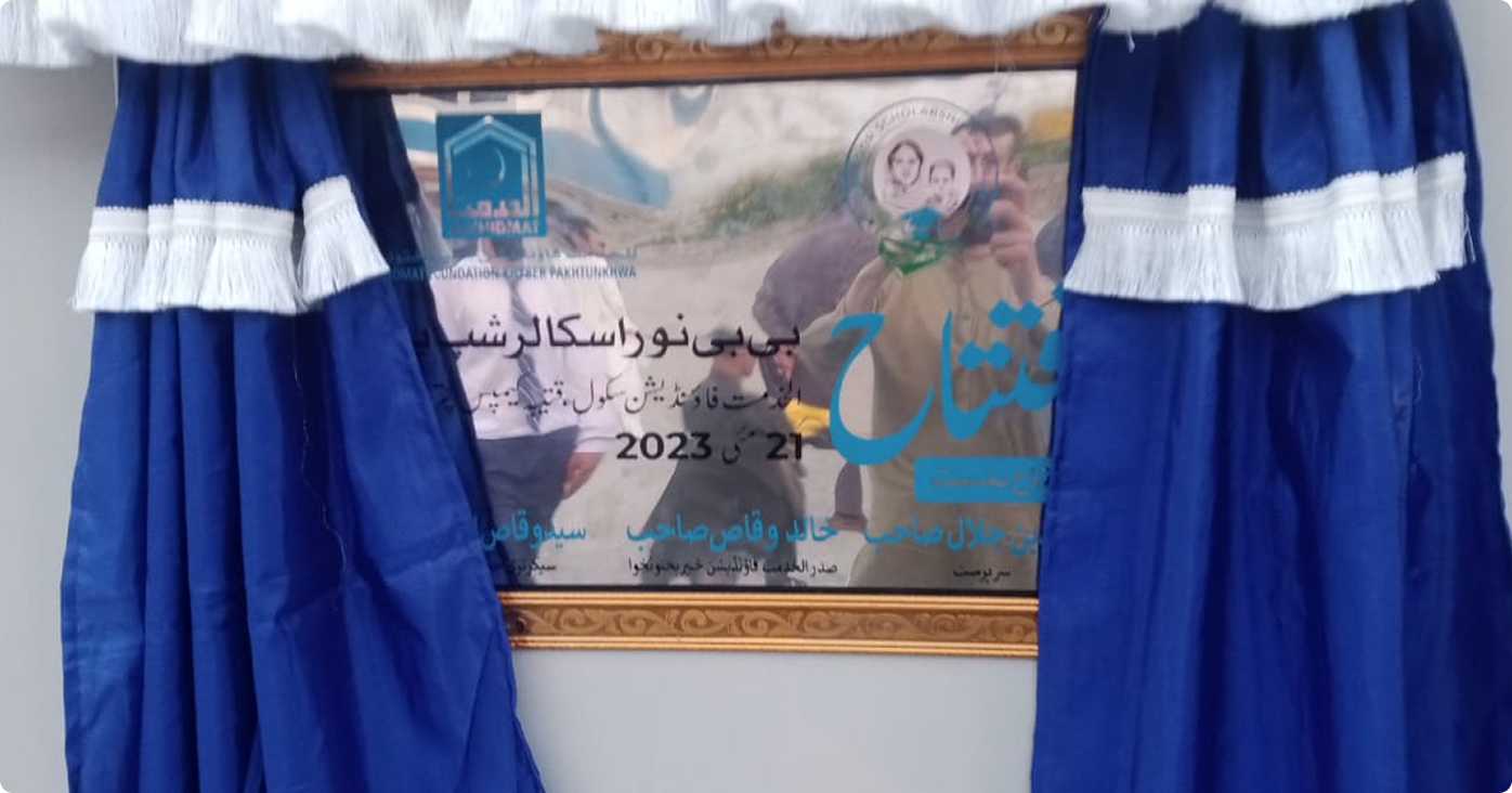 Blue curtains with white fringes framing a commemorative plaque in Urdu celebrating an event held on May 21, 2023.