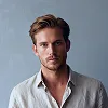 Retrato de un hombre con el pelo corto y camisa blanca sobre un fondo gris.