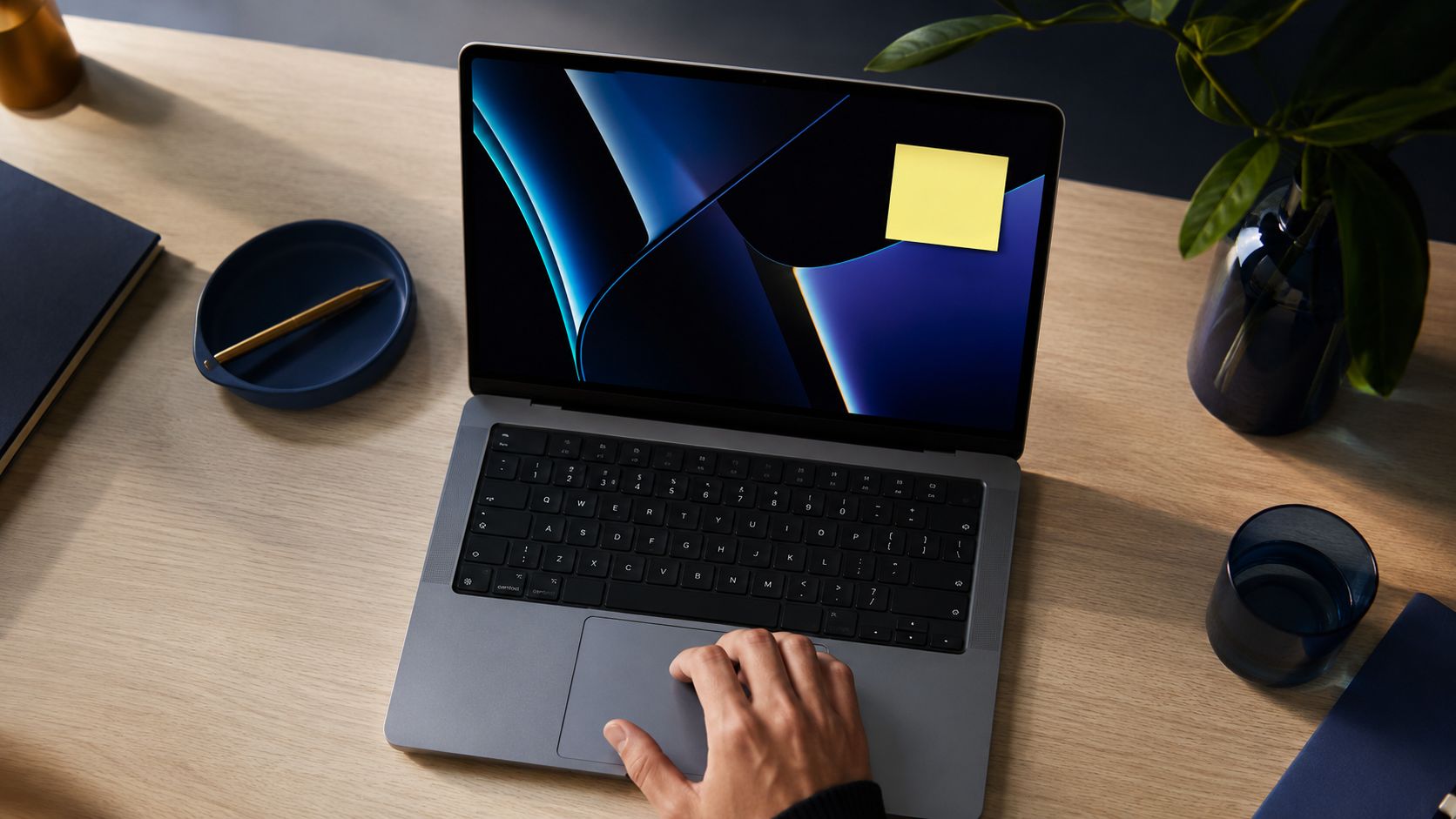 Ręka obsługująca gładzik laptopa z żółtą karteczką samoprzylepną na ekranie, stojącym na biurku