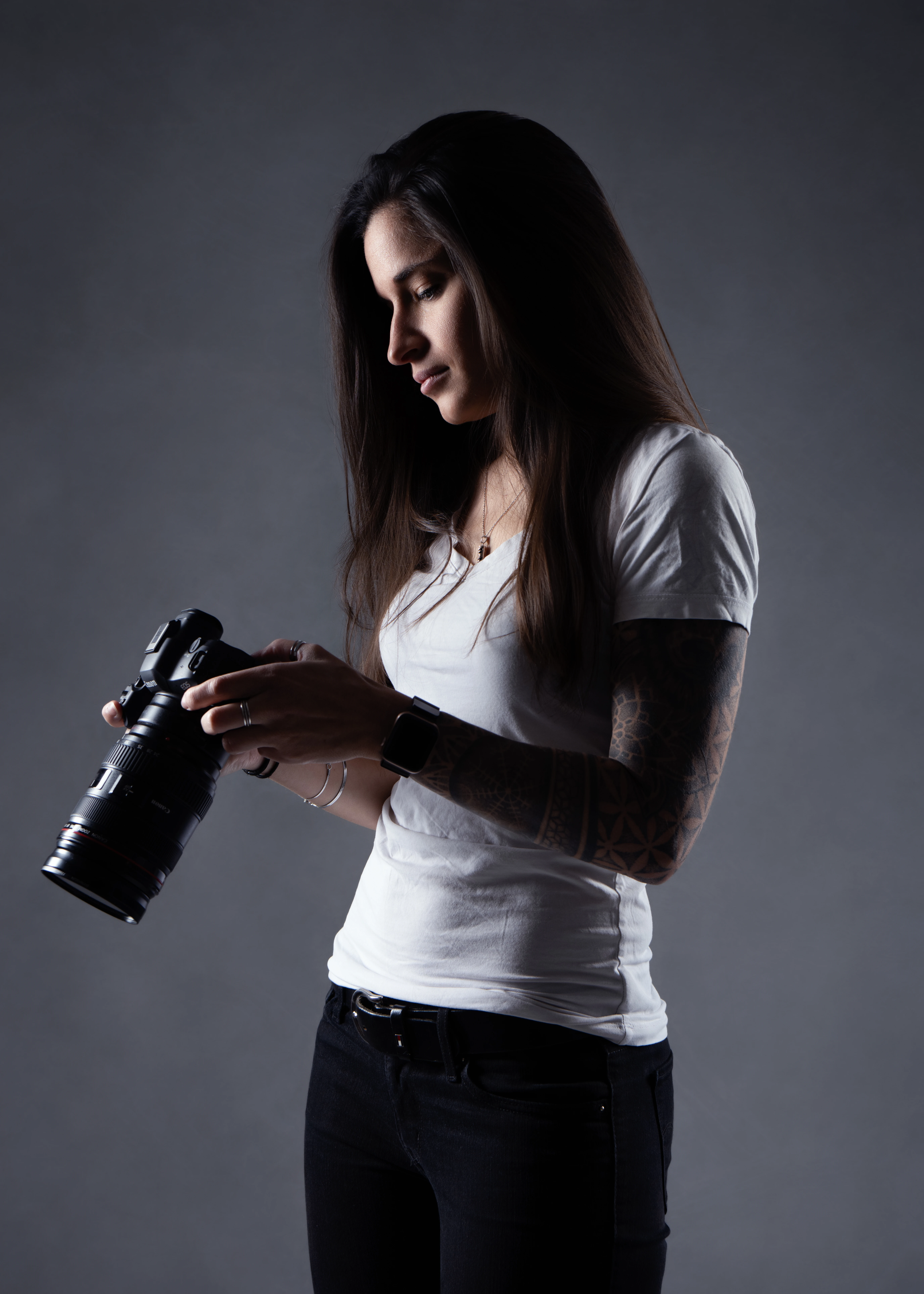 Une femme avec un tatouage sur le bras gauche se tient dans la rue et prend une photo avec un appareil photo reflex numérique.