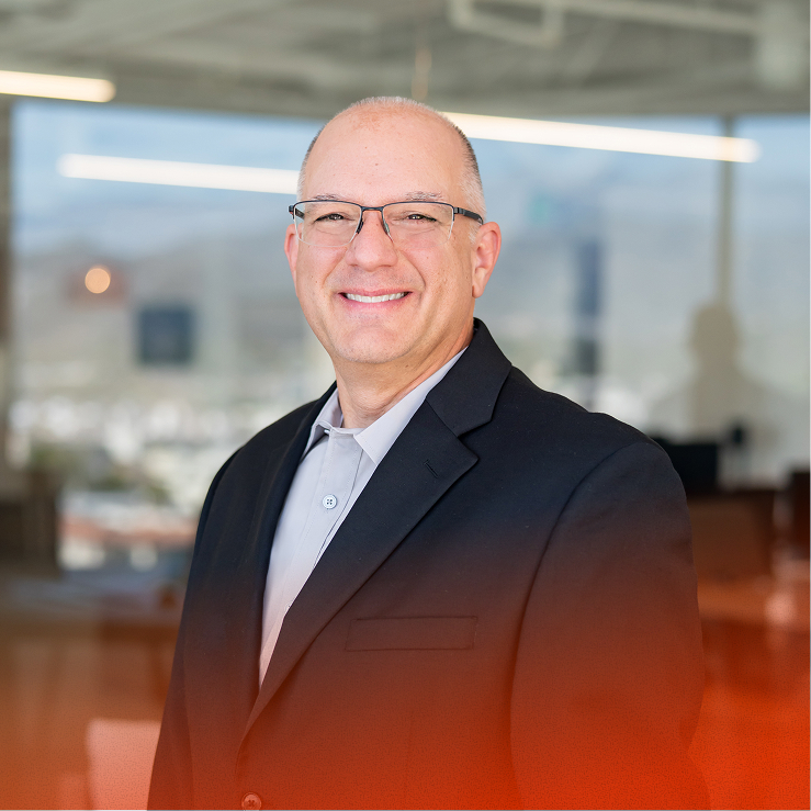 Smiling man in glasses and suit standing in a bright office.