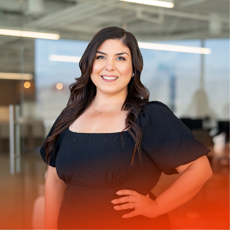 Woman smiling, hand on hip, posing in a modern glass-walled office.