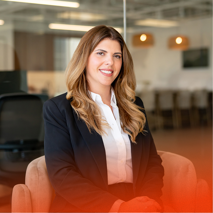 Woman smiling, seated in an office chair, modern open-plan workspace.