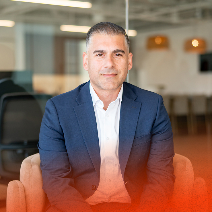 Man in suit sits facing camera in modern office lounge.