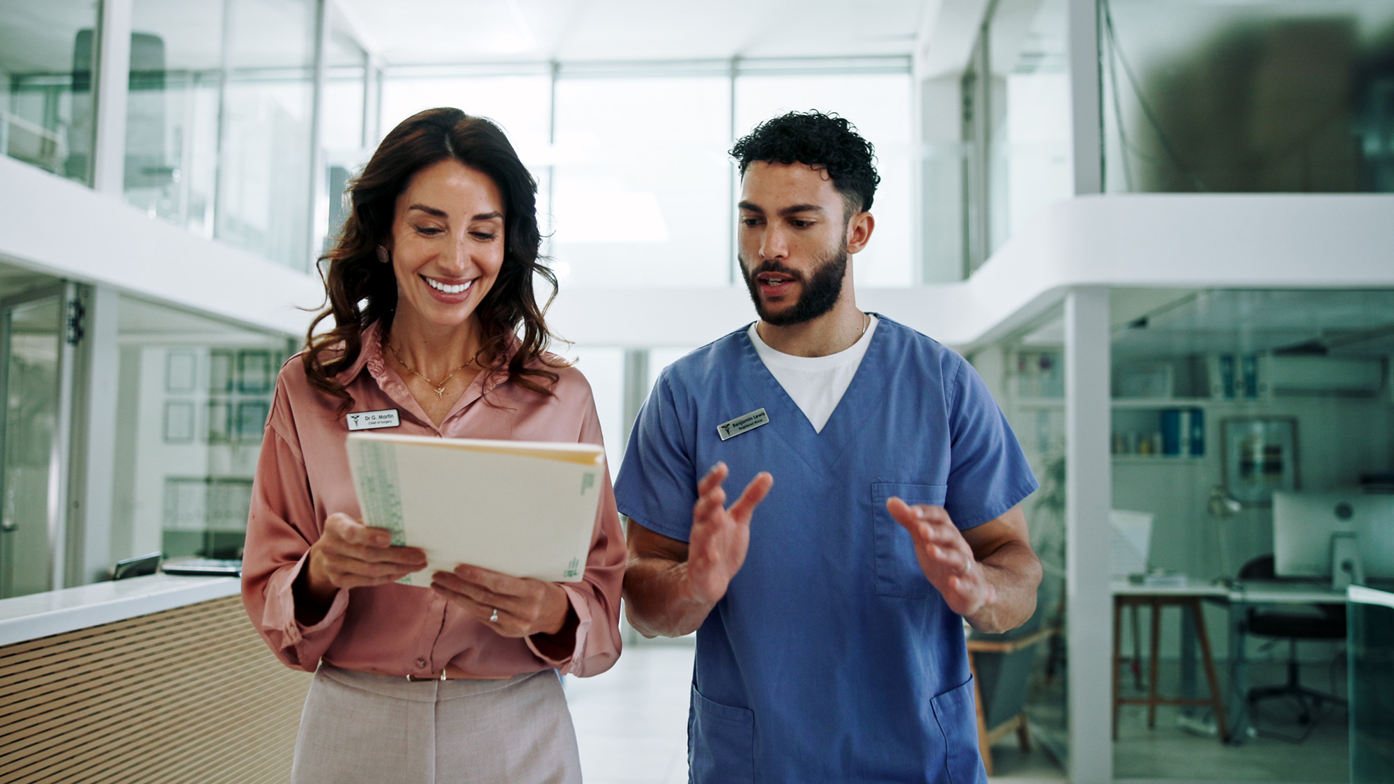 Doctor holding folder; nurse gesturing while walking in clinic
