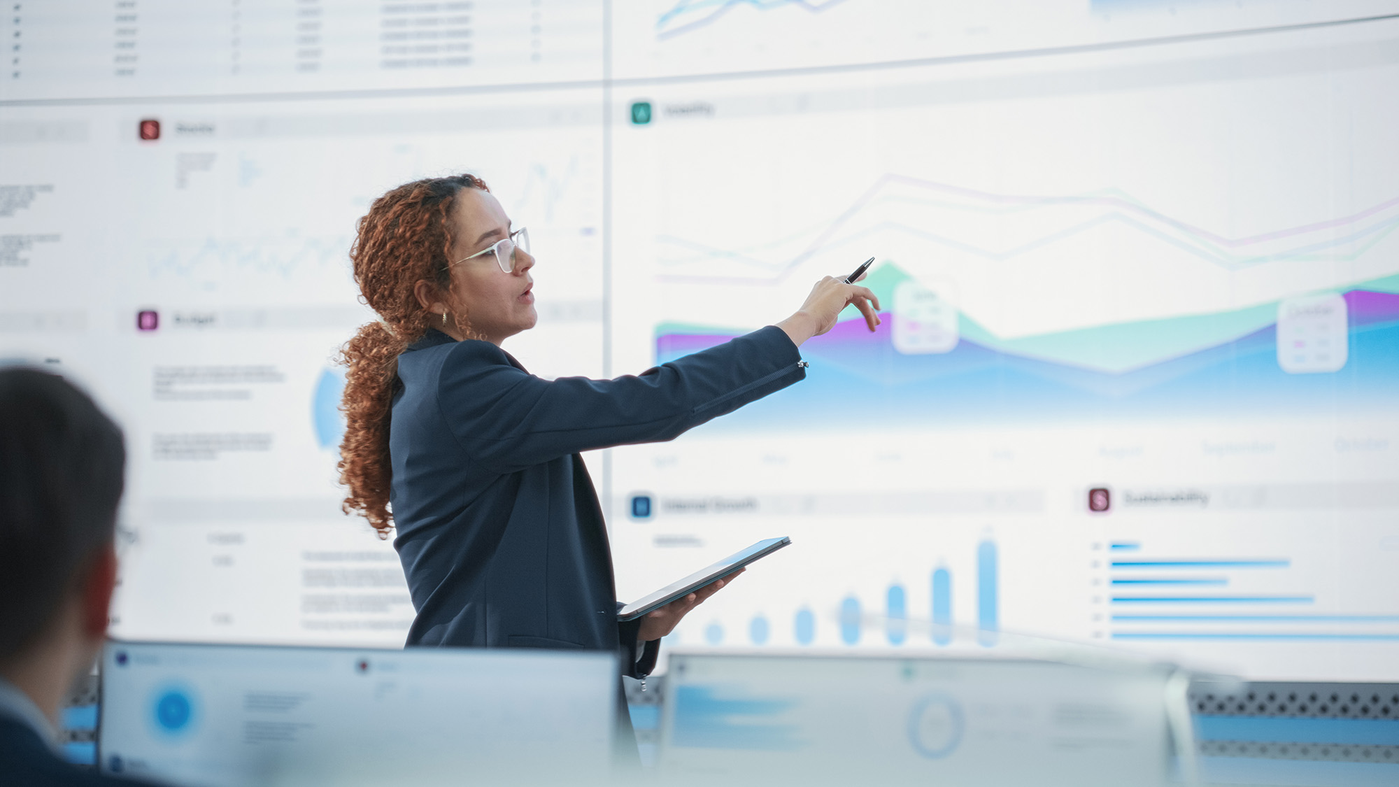 Presenter points at data charts on a large screen in a meeting room