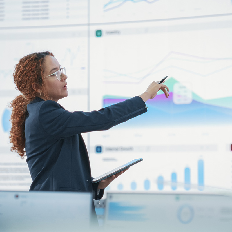 Presenter pointing at sales charts on large screen in conference room