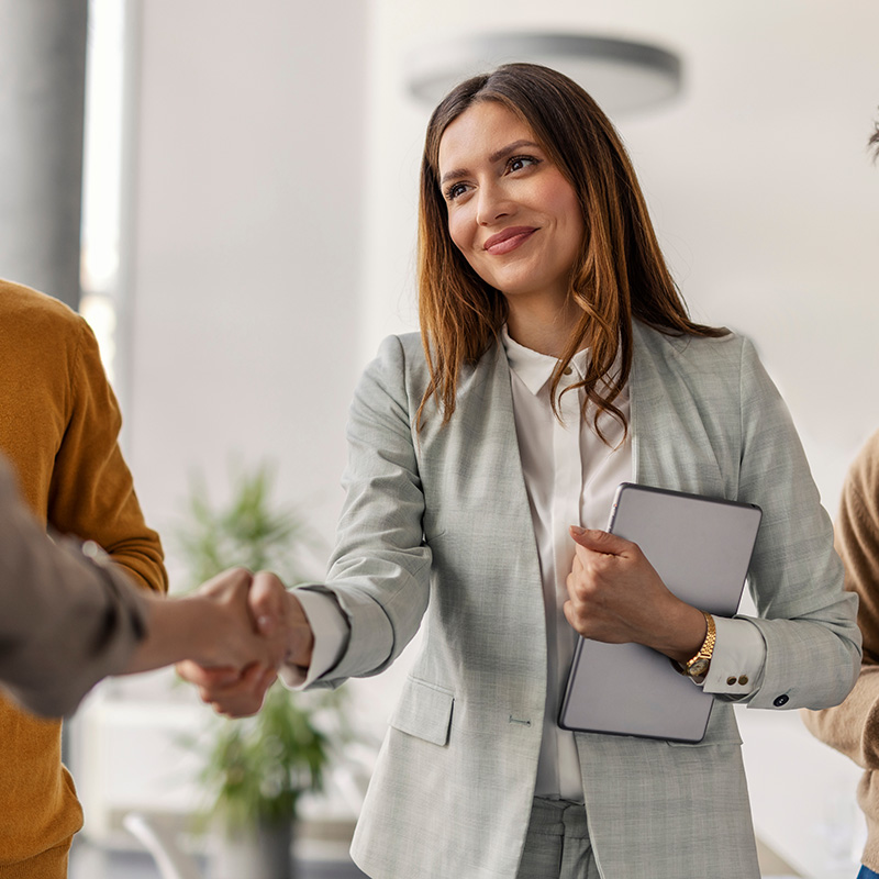 Businesswoman shaking hands, holding tablet in modern office setting