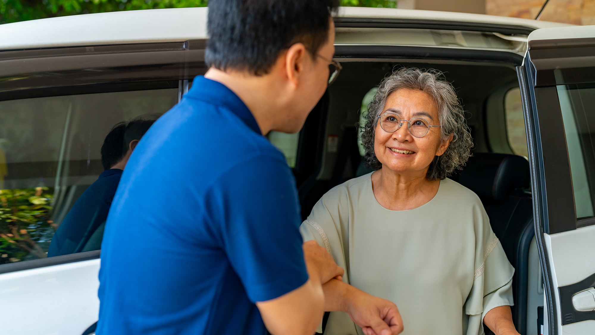 Elderly woman smiling as a man helps her out of a car
