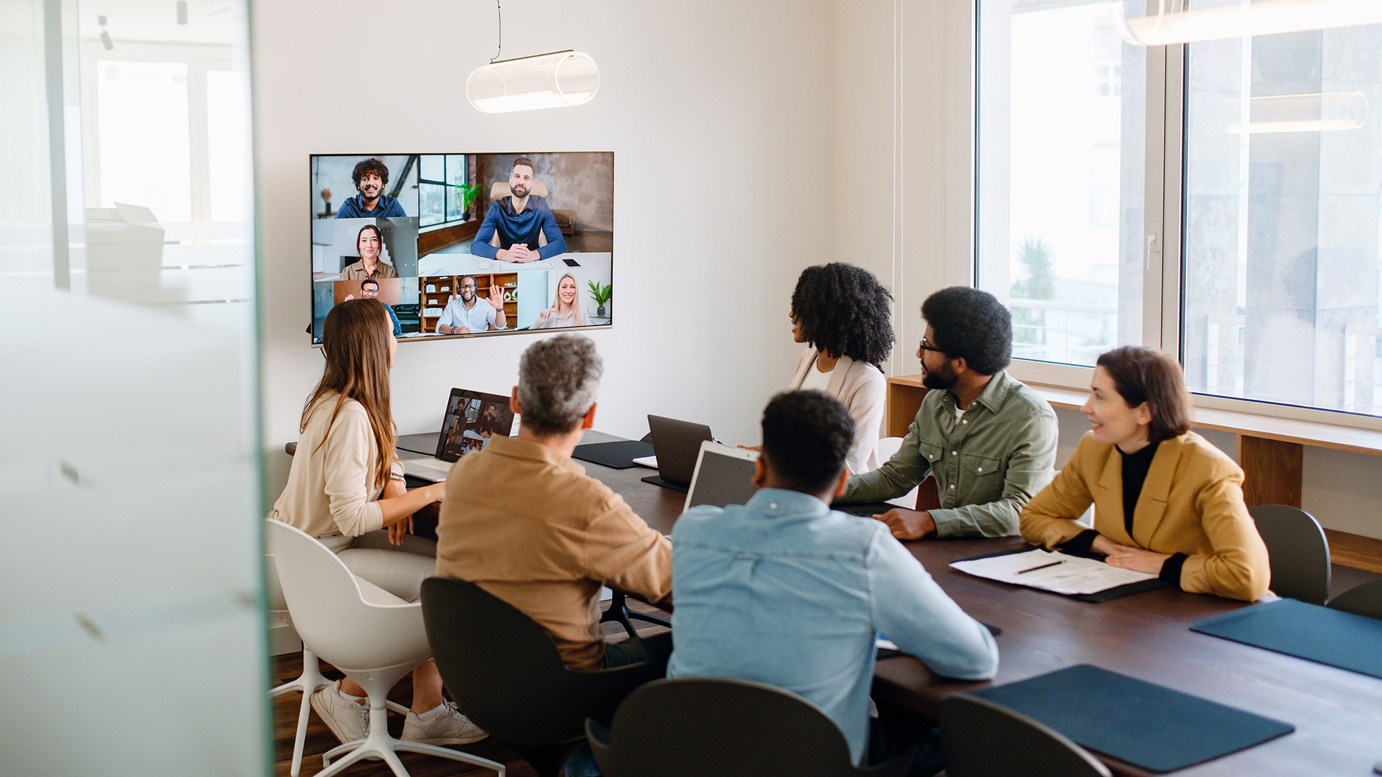 Team watching a video call on a wall screen in a conference room