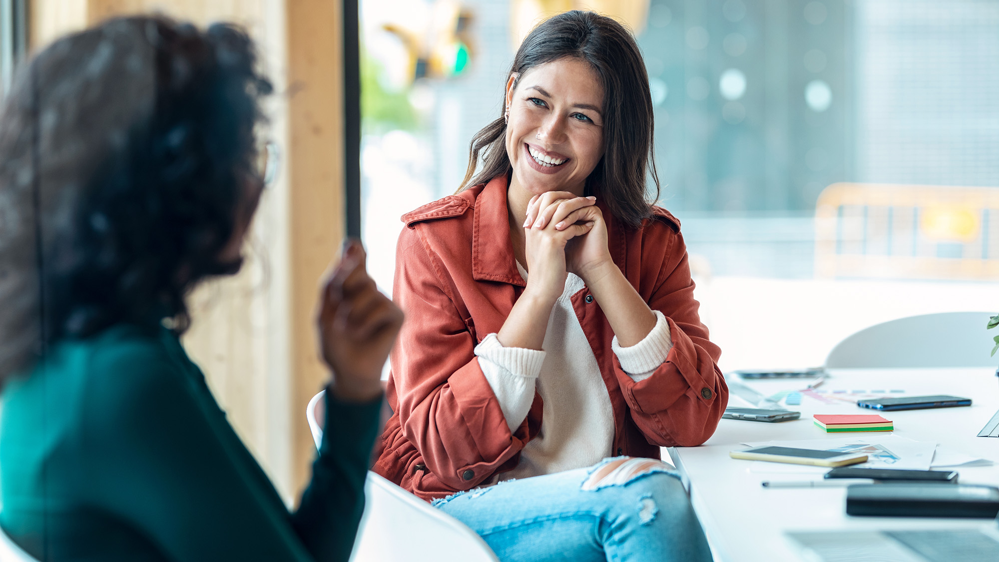 Young woman smiling, listening to colleague across a bright office.