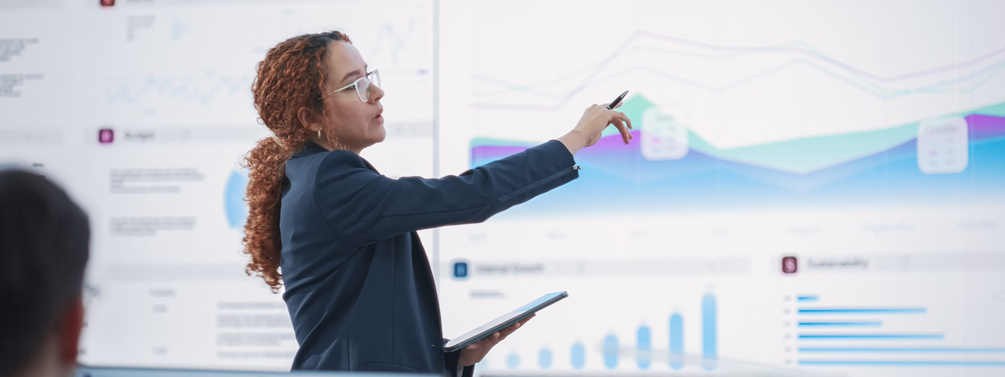 Presenter points at data charts on a large screen in a meeting room