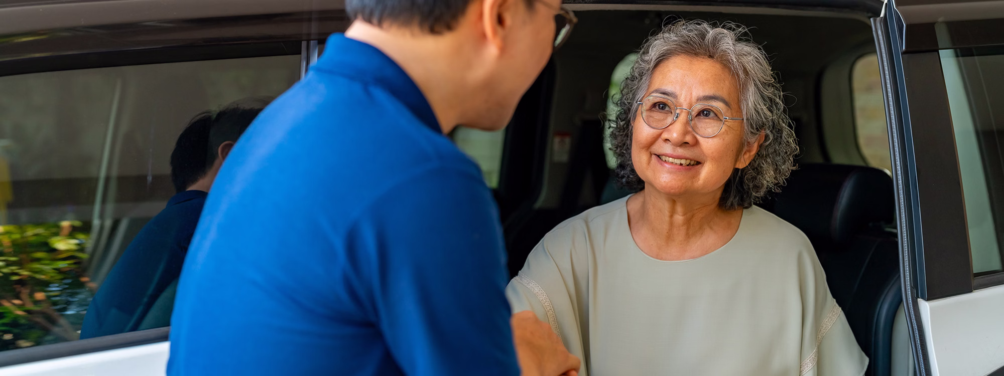 Elderly woman smiling as a man helps her out of a car