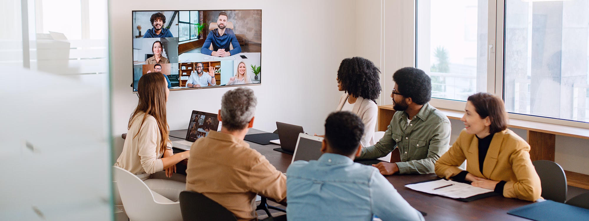 Team watching a video call on a wall screen in a conference room