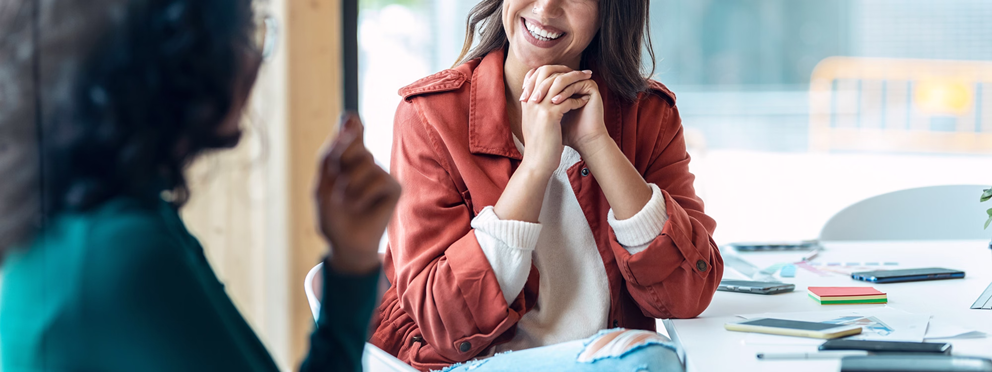 Young woman smiling, listening to colleague across a bright office.