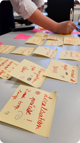 Hand writing on sticky notes with red ink scattered on a gray table in a brainstorming session.