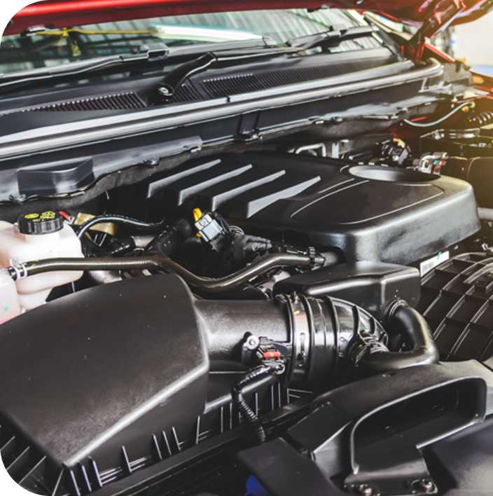Close-up of a modern car engine compartment with various hoses, air intake components, and plastic covers under an open hood.
