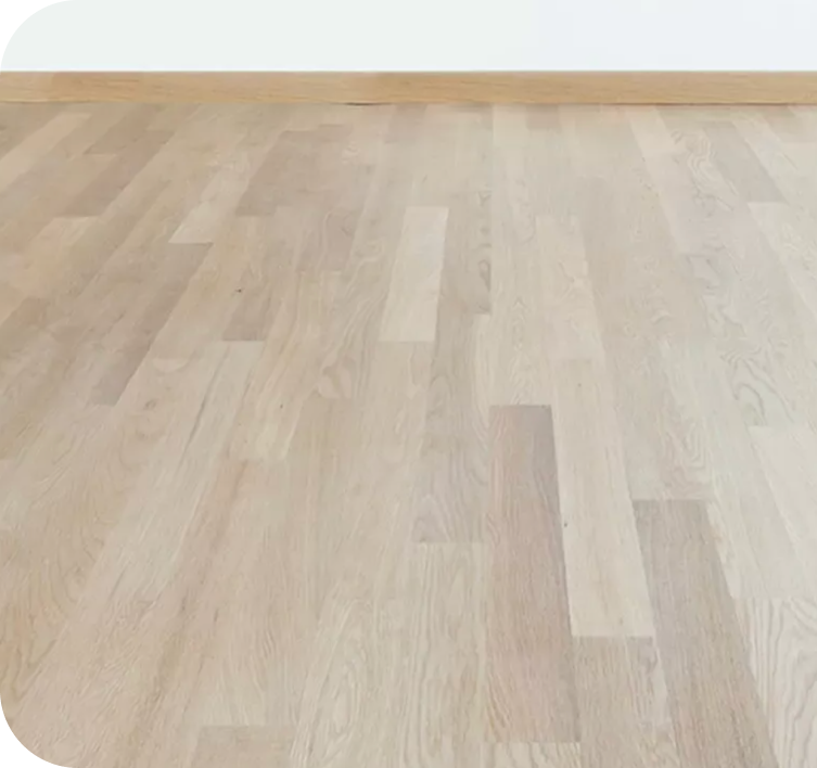 Light wood flooring with visible grain patterns and a wooden baseboard against a white wall.
